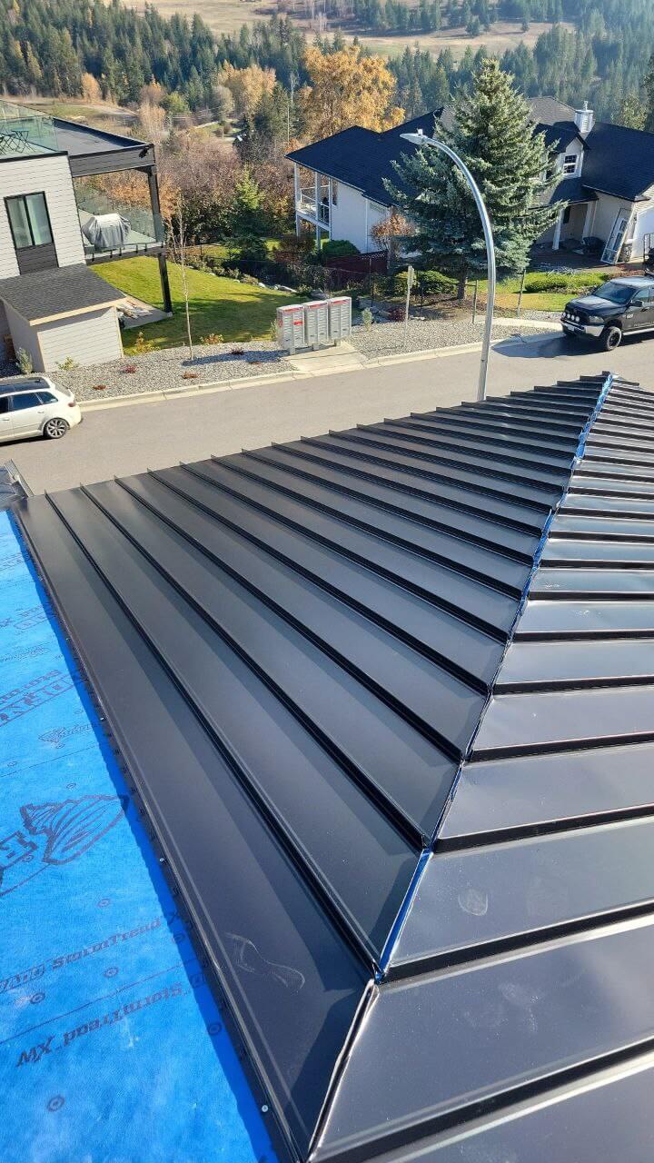 Professional Roof Installation In Progress – Vernon, BC Roofers installing standing‑seam metal panels on a sloped roof; visible workers with safety gear.